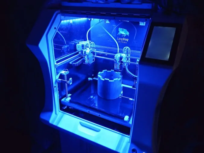 FDM-3D-Drucker mit blauer Innenbeleuchtung beim Druck eines Orthesen-Bauteils